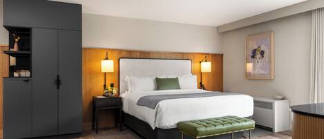 A modern hotel room with a large bed, bedside lamps, a green bench, a wardrobe, and a desk with a lamp.