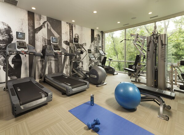A modern gym with treadmills, elliptical machines, and free weights, featuring large windows and a mural on the wall. - The Watershed (Norwalk)