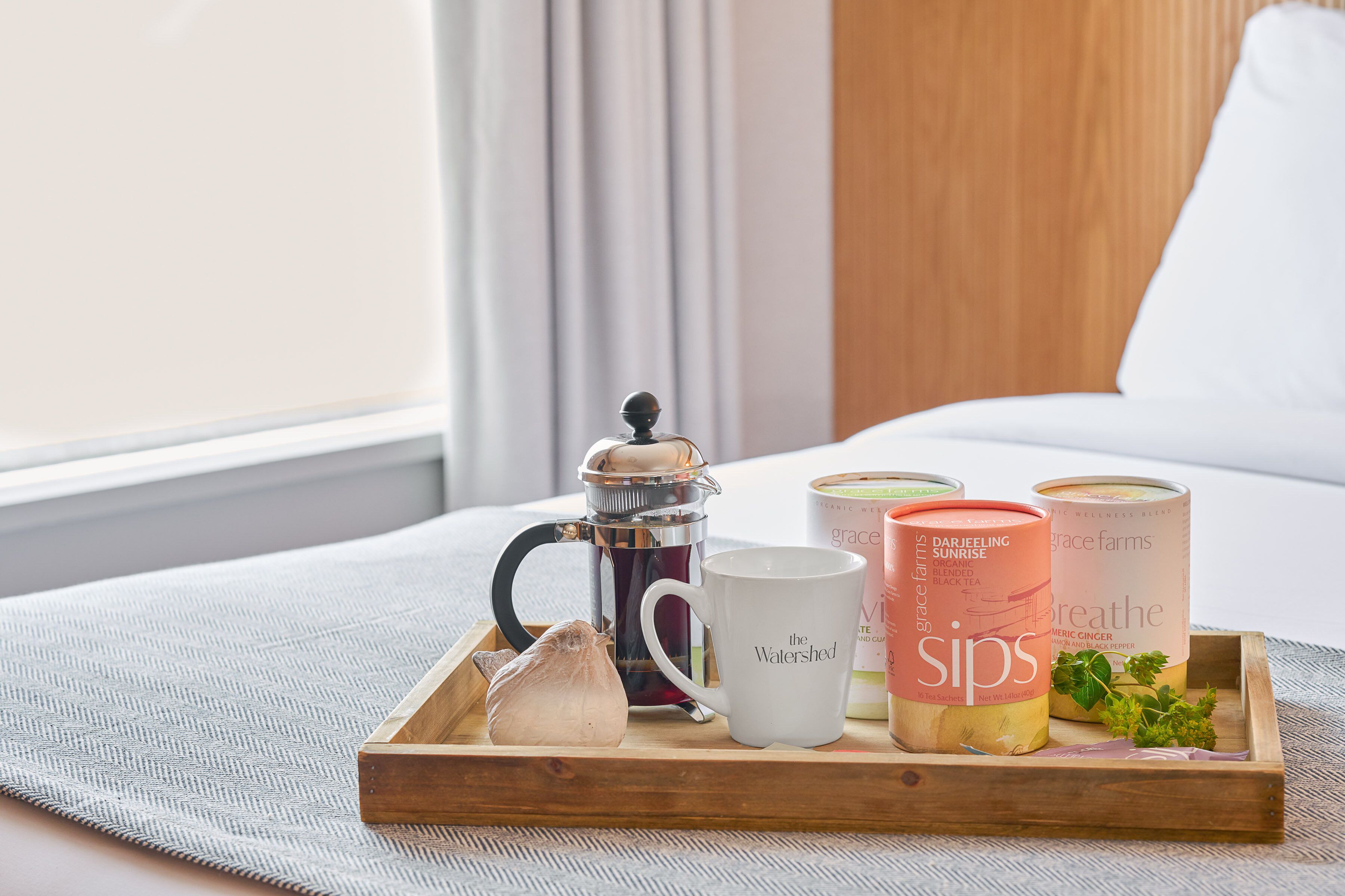 A tray with a coffee pot, a mug, and three candles on a bed.