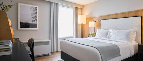 Habitación de hotel con una cama grande, un escritorio con una silla, un cuadro en la pared y una ventana con cortinas.