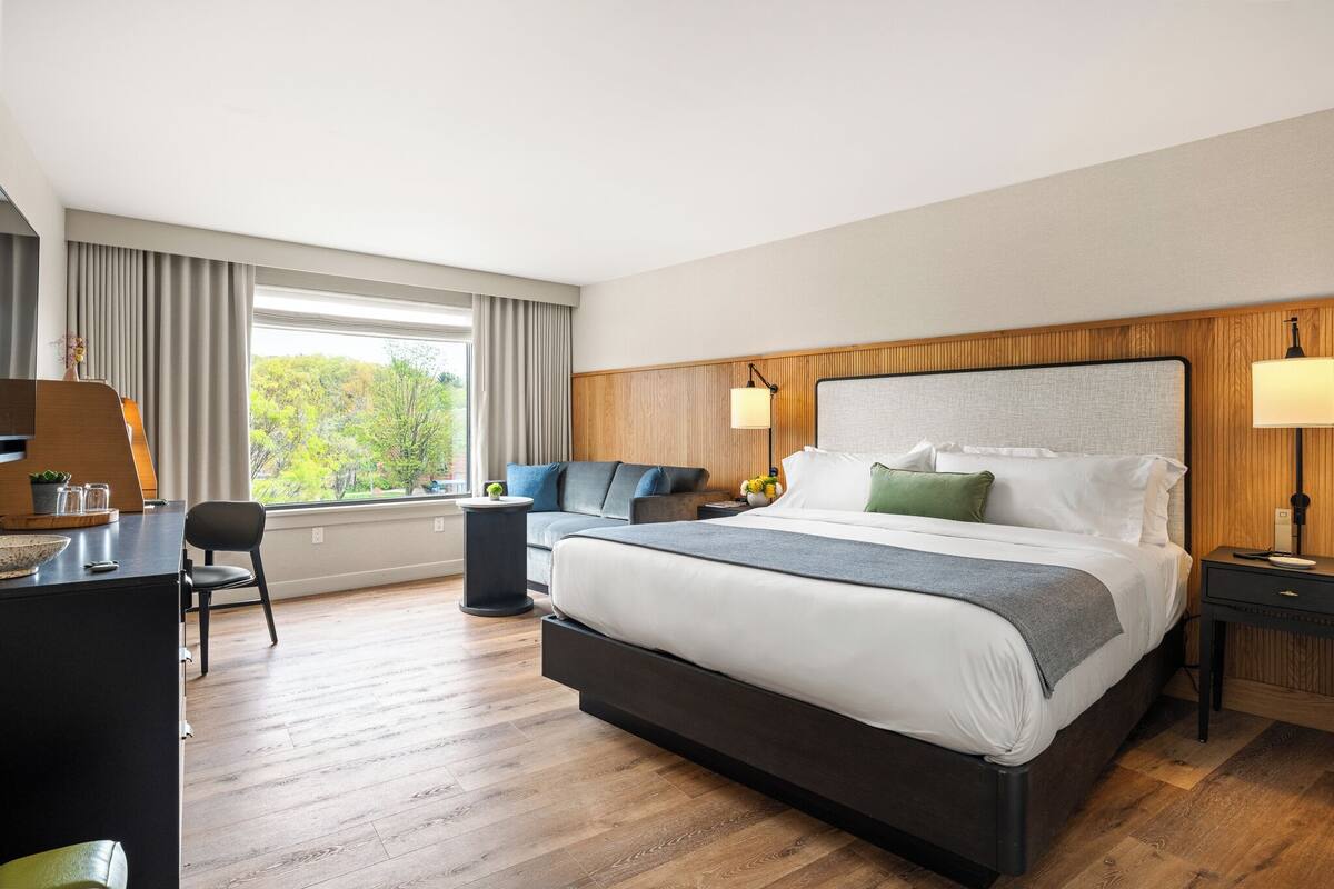 A modern hotel room with a large bed, a desk, and a sofa.