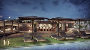An outdoor pool area with lounge chairs, a bar, and string lights. - The Watershed (Norwalk)