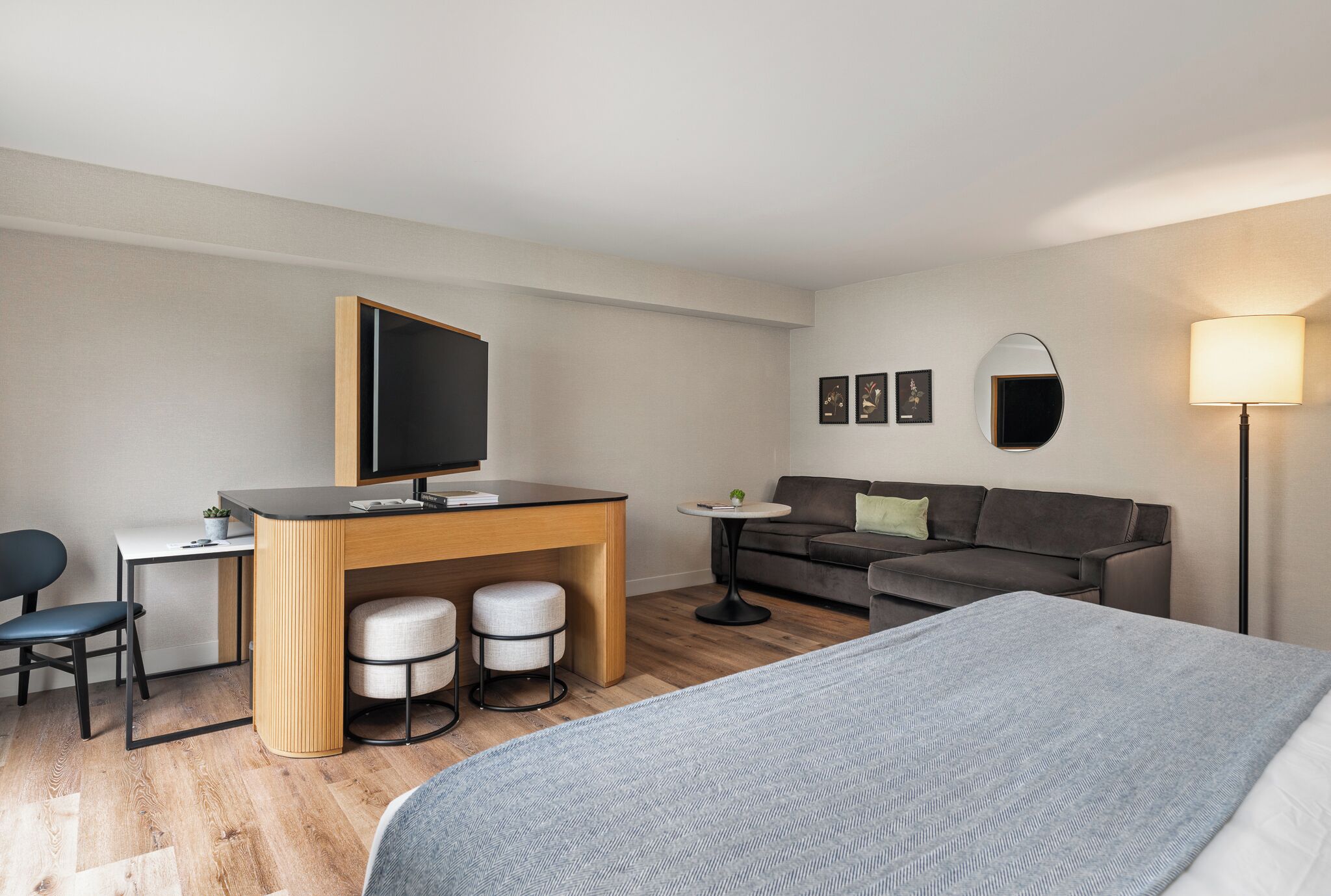 Et moderne hotelværelse med seng, skrivebord med computer, sofa og et lille bord med lampe.