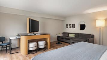 Et moderne hotelværelse med seng, skrivebord med computer, sofa og et lille bord med lampe.
