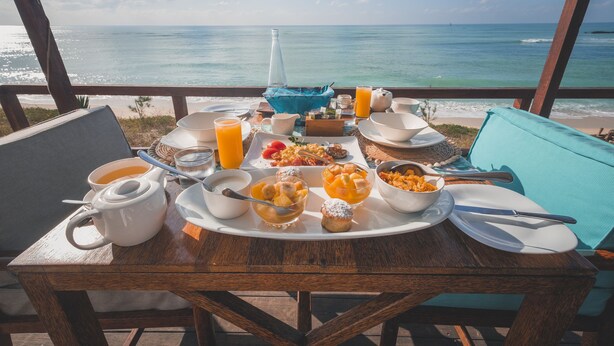 A breakfast table with various dishes and a view of the ocean.