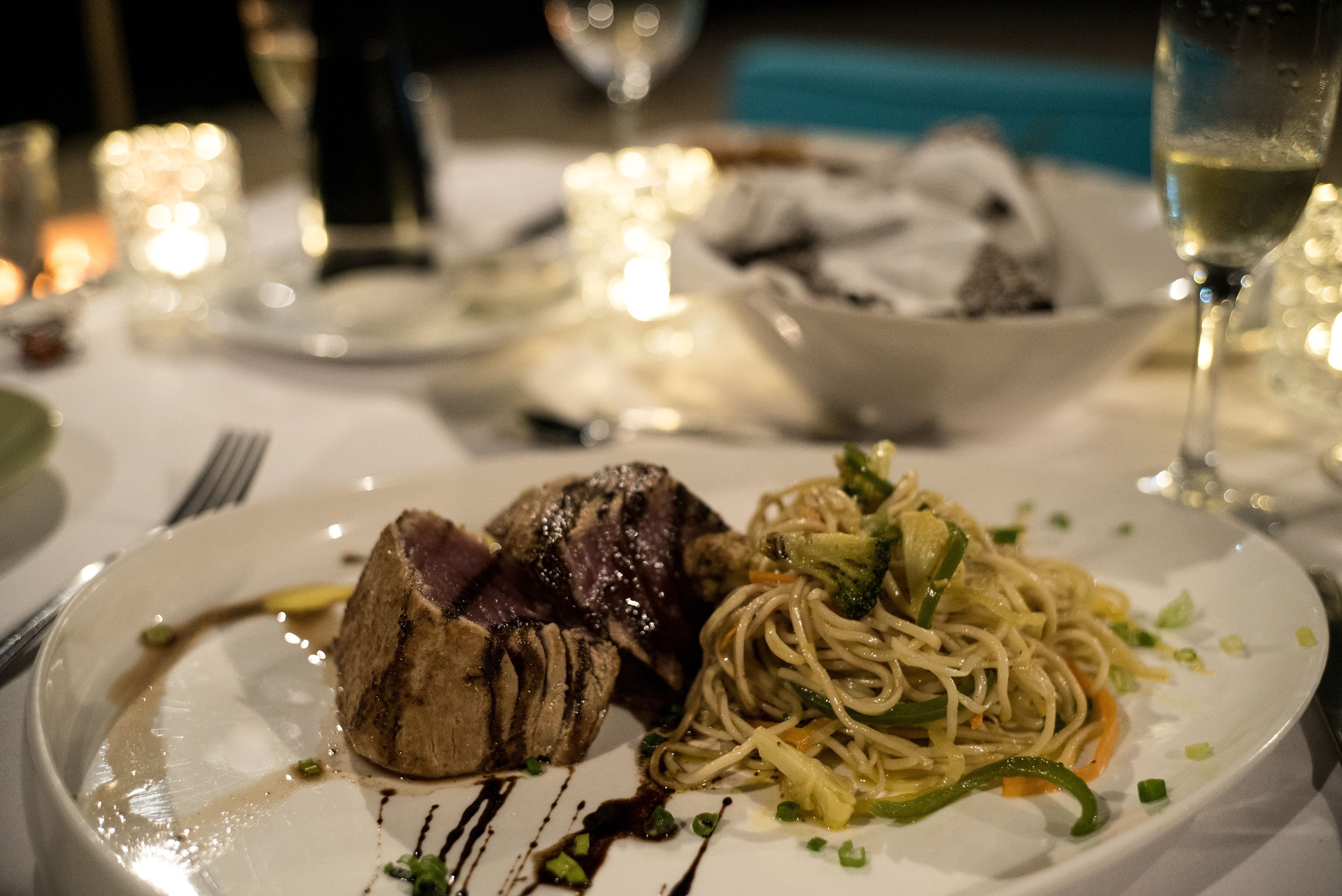 Une assiette de nourriture comprenant un steak et des nouilles, un verre de vin et des bougies sur une table.