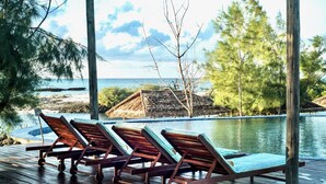 A wooden deck with lounge chairs facing a pool and ocean view.
