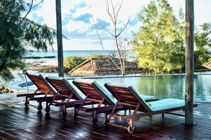 A wooden deck with lounge chairs facing a pool and ocean view.