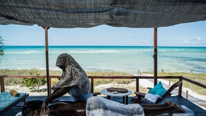 A beachside massage area with a view of the ocean, wooden deck, and lounge chairs.