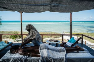 A beachside massage area with a view of the ocean, wooden deck, and lounge chairs.