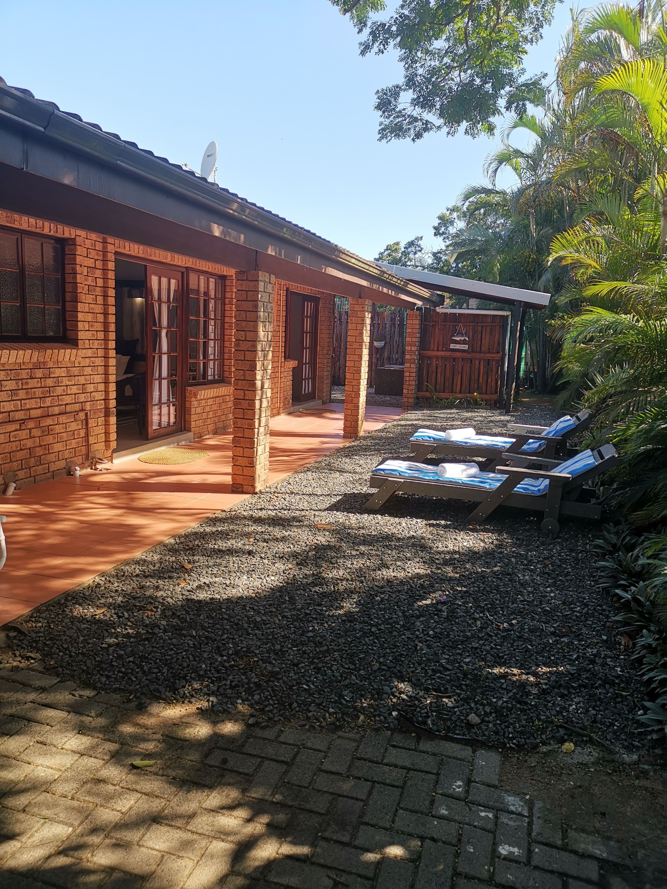 A brick building with a covered patio area, a gravel path, and lounge chairs.