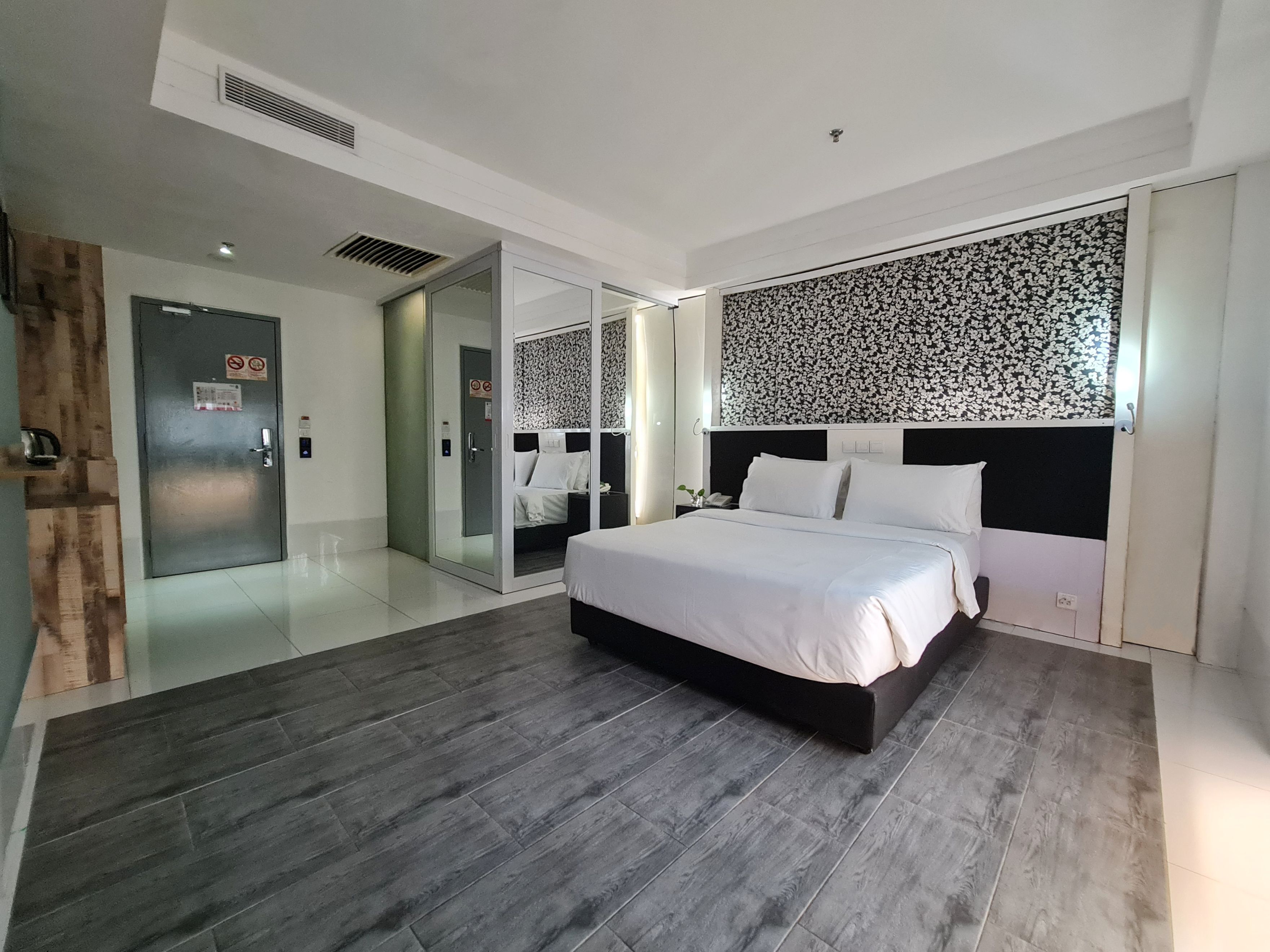 A modern hotel room with a large bed, a glass door leading to a bathroom, and a patterned wall above the bed.