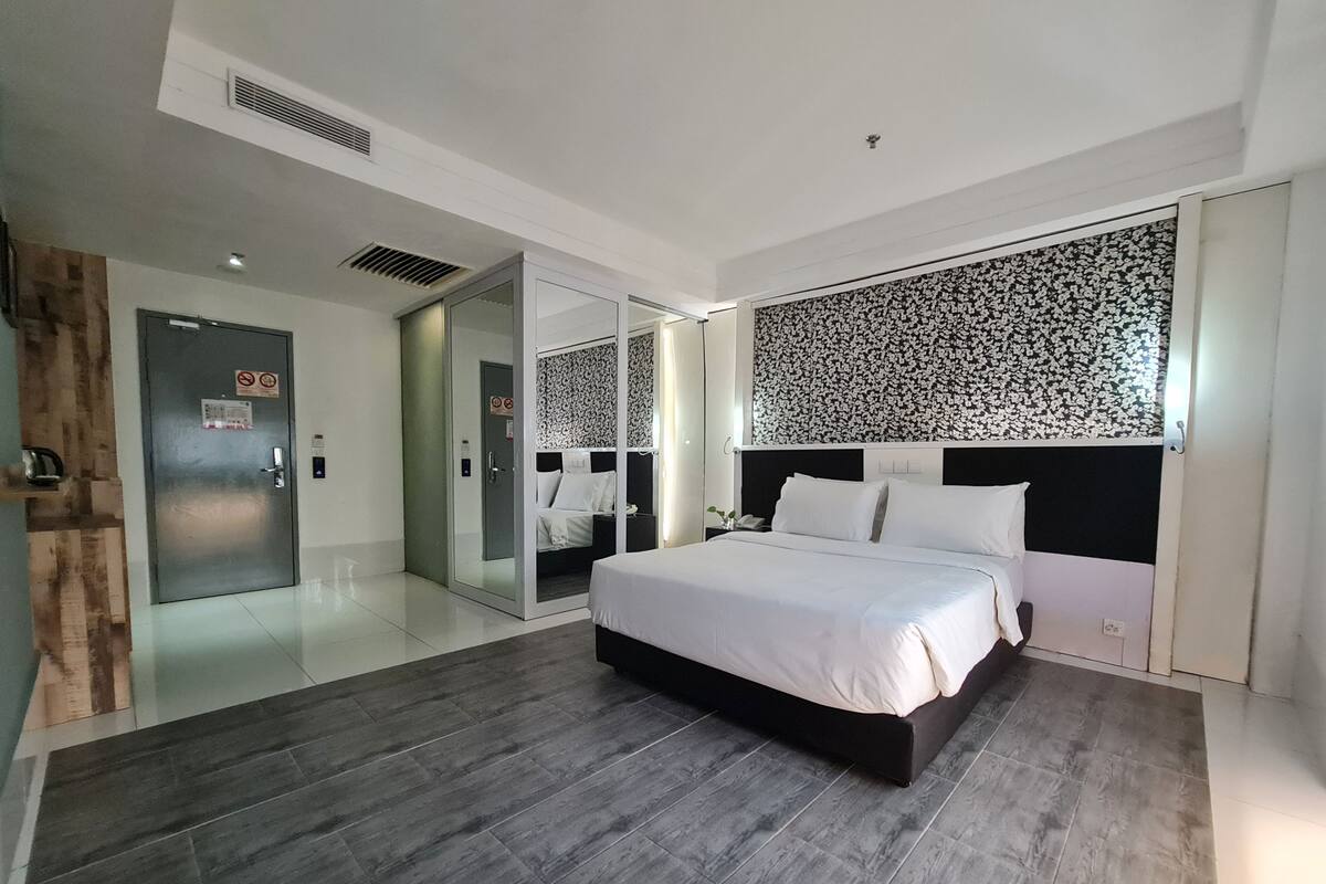 A modern hotel room with a large bed, a glass door leading to a bathroom, and a patterned wall above the bed.
