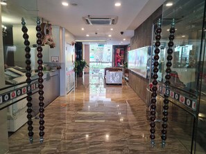 A hotel lobby with a polished marble floor, glass partitions with decorative bead curtains, and a reception desk with a digital display.