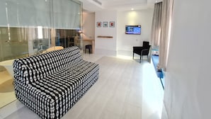 Ein modernes Wohnzimmer mit einem gemusterten Sofa, einem an der Wand montierten Fernseher und einer Glaswand.