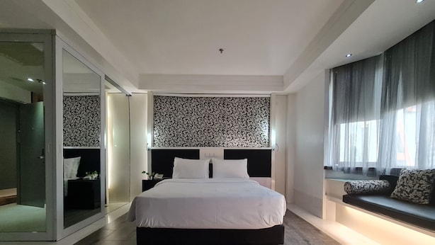 Ein modernes Schlafzimmer mit einem großen Bett, einer Glastür zu einem begehbaren Kleiderschrank, einem gemusterten Kopfteil und einem Fenster mit Aussicht.
