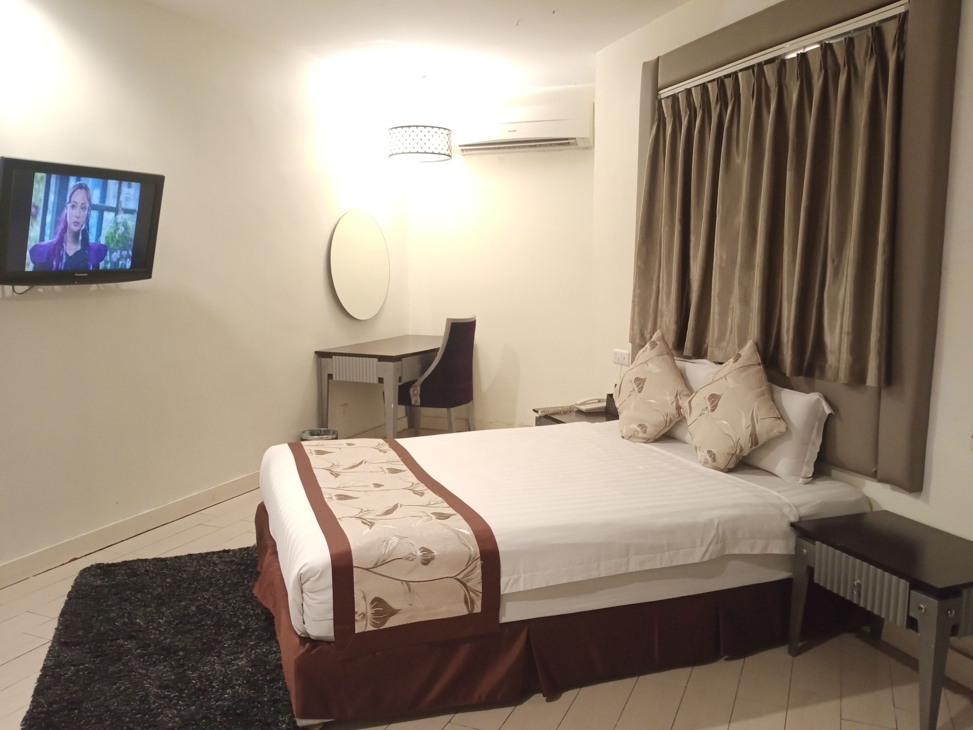 Een hotelkamer met een bed, een bureau, een stoel, een televisie en een raam met gordijnen.
