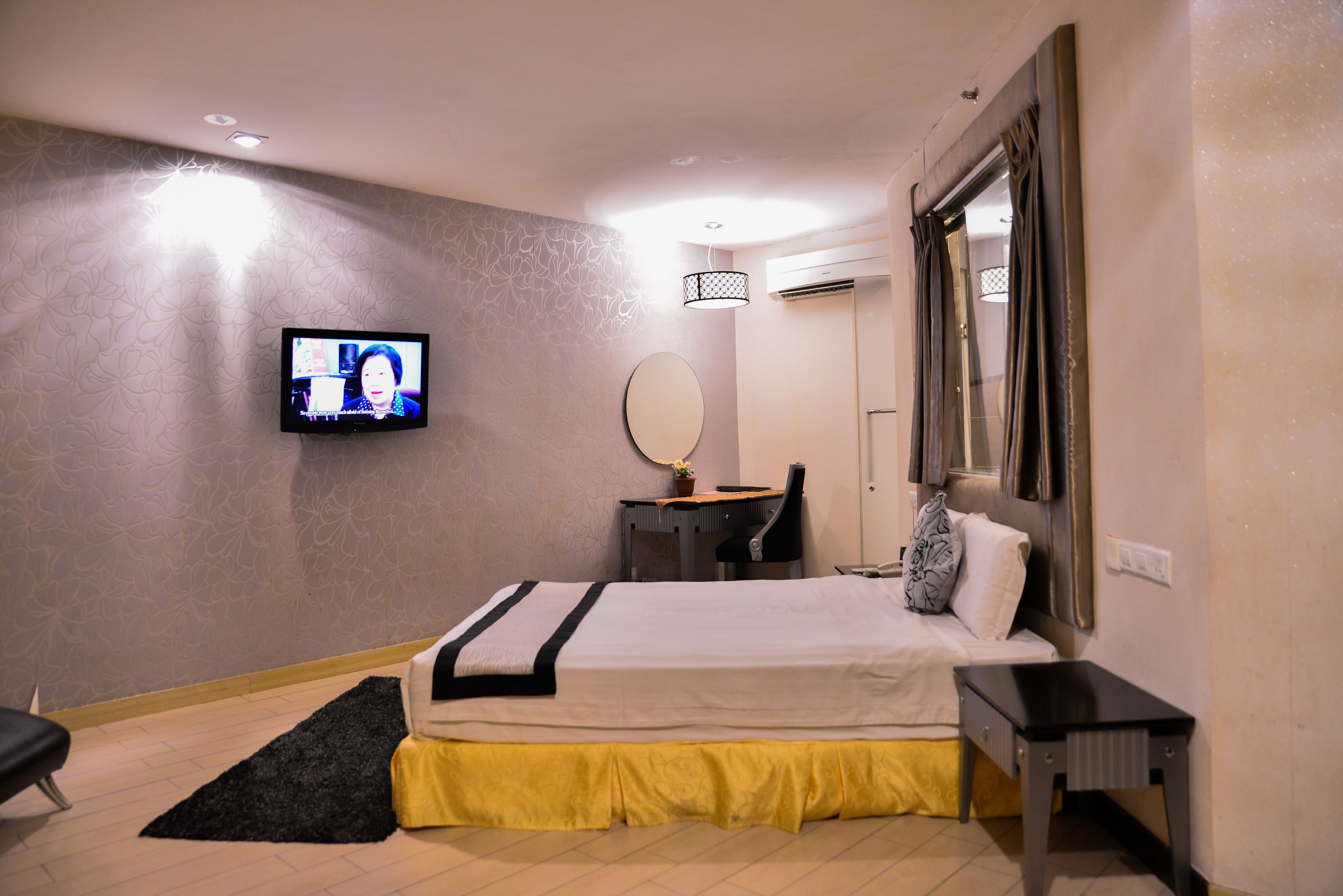 Une chambre d’hôtel équipée d’un lit, d’un bureau, d’une chaise, d’une télévision, d’un miroir et d’un appareil de climatisation.