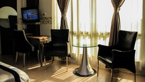 Habitación de hotel con zona de comedor, dos sillas, una mesa de vidrio y televisor en la pared.