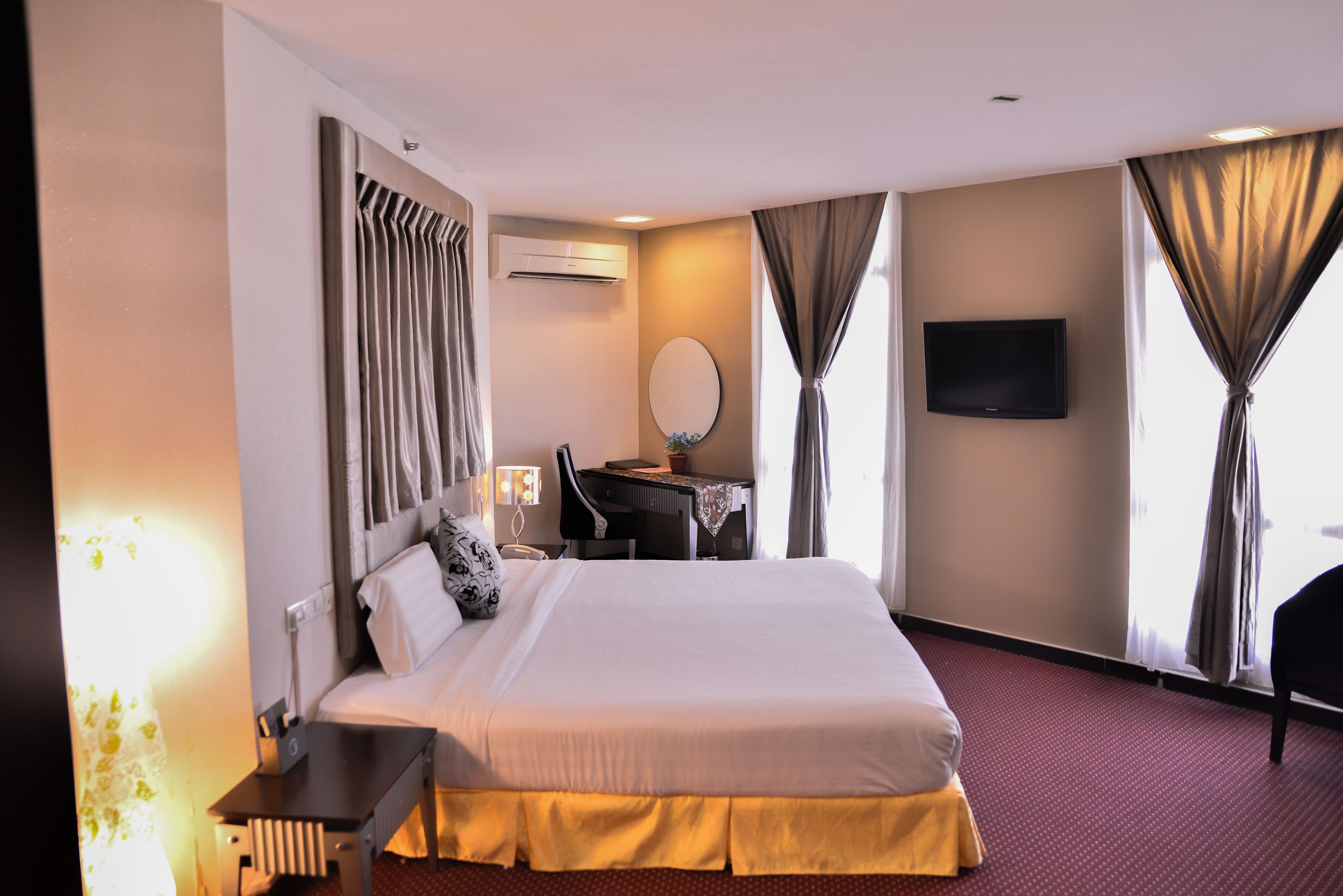 A hotel room with a large bed, a desk with a chair, a flat-screen TV, and a window with curtains.