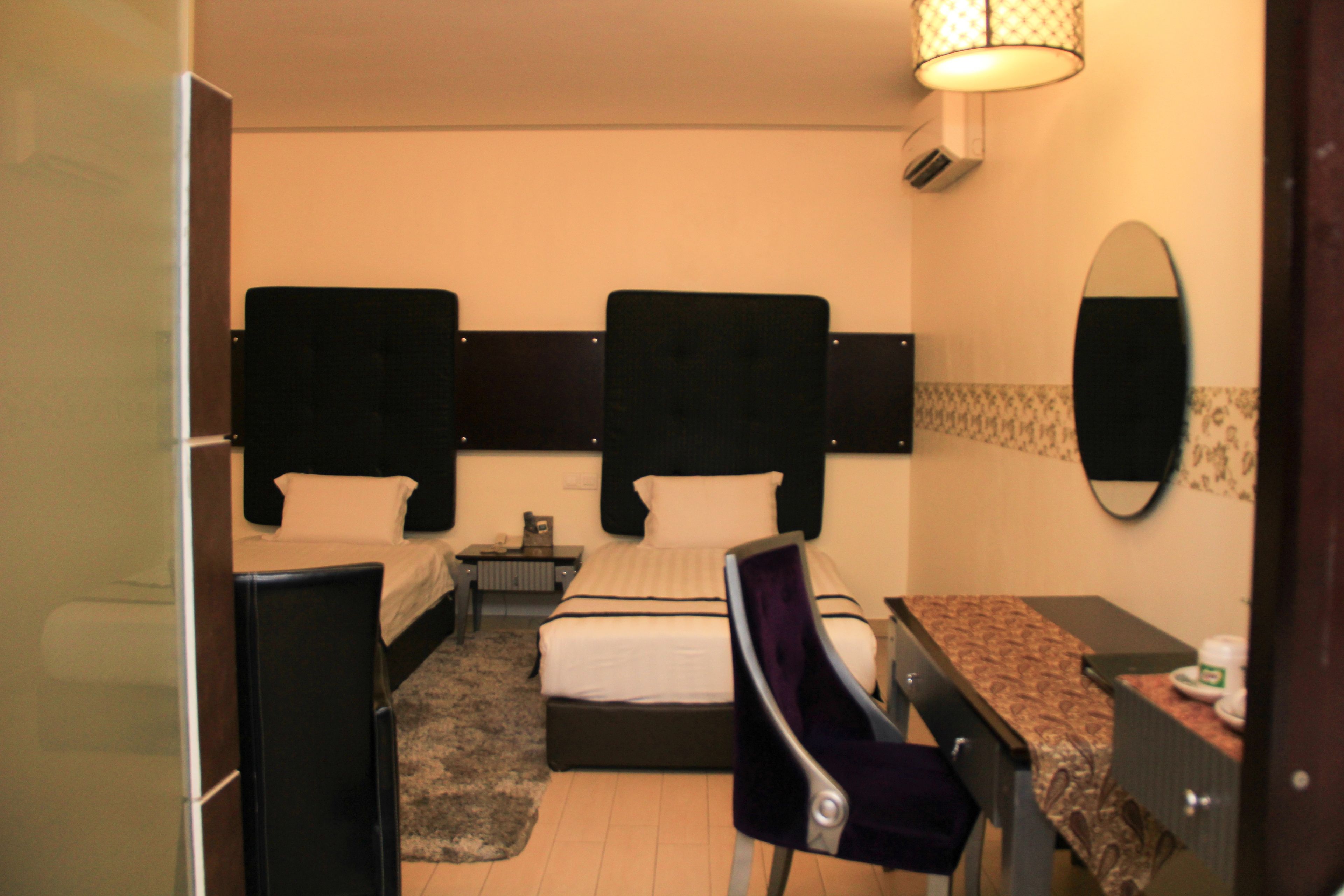 A compact hotel room with two beds, a desk, a chair, a mirror, and a small table.