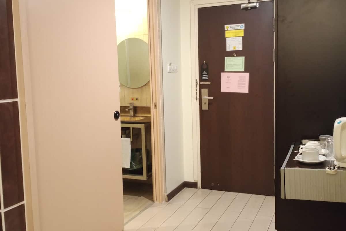 Habitación de hotel con puerta de madera, un baño pequeño con espejo y una mesita de noche con taza y plato.