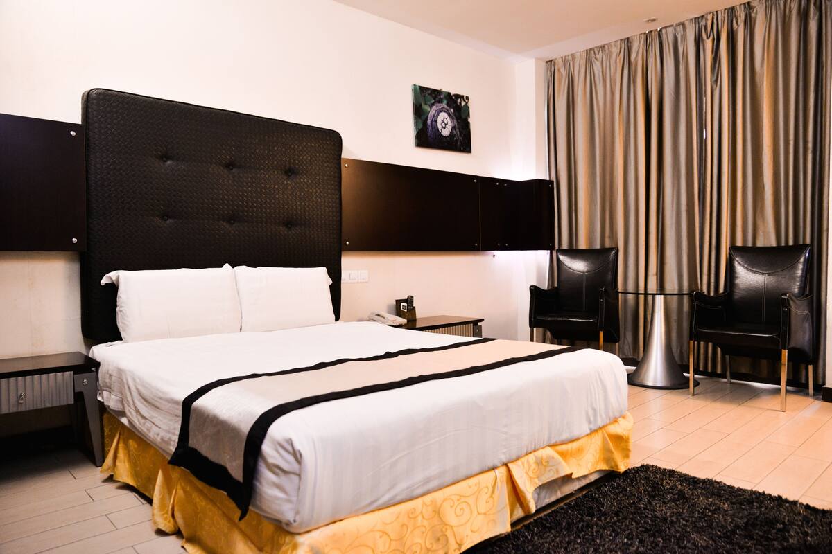 Una habitación de hotel con una cama grande, una mesita de noche, una lámpara y dos sillas.