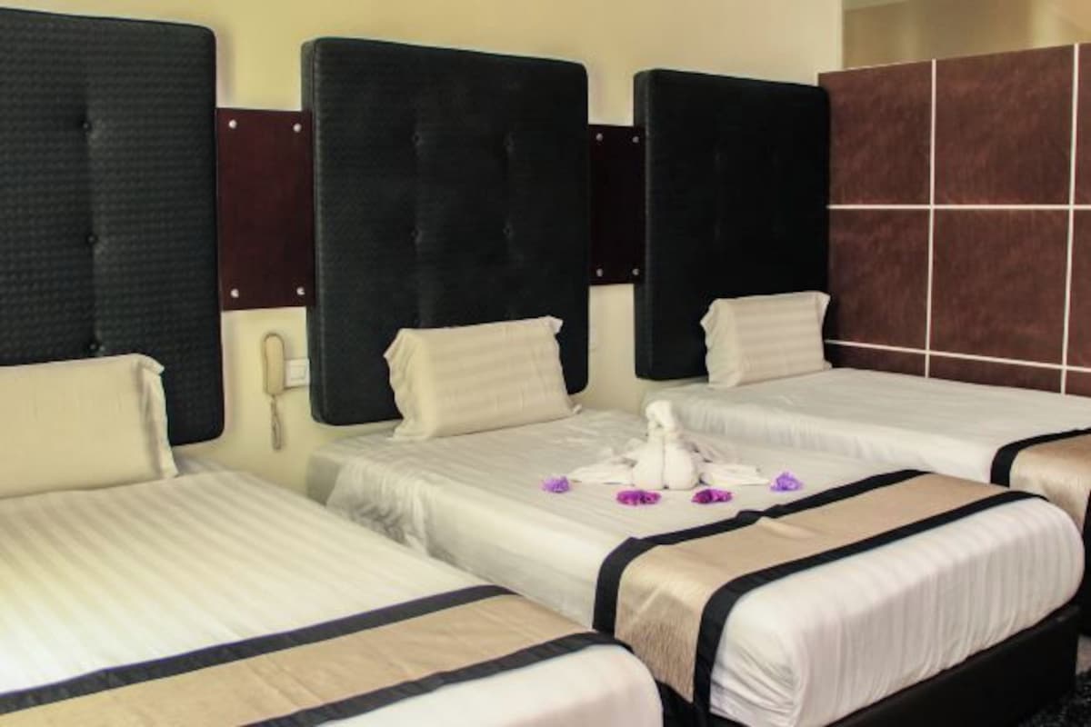 A hotel room with three beds, each with a black headboard and white bedding. There is a telephone on the wall next to the beds.