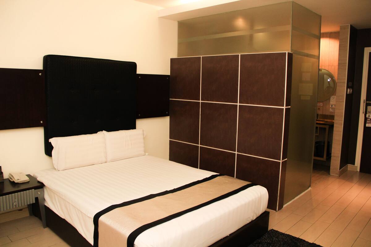 Habitación de hotel con una cama grande, un cabecero oscuro, un armario con espejo y una mesita con teléfono.