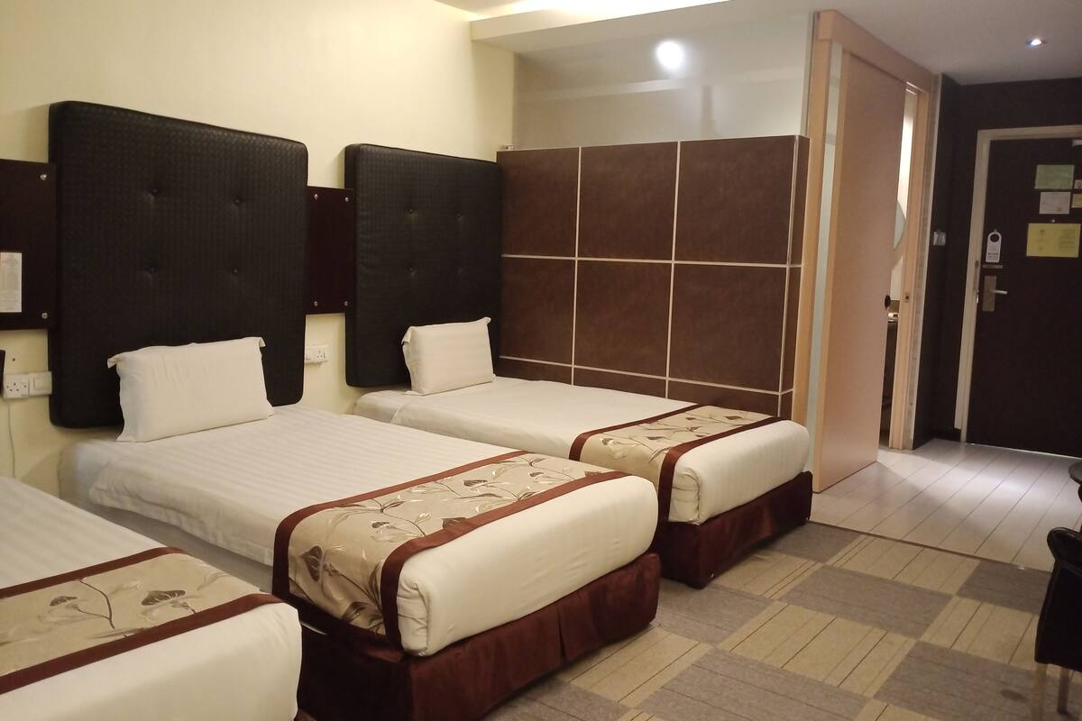 Habitación de hotel con dos camas, cabecera oscura, pared de azulejos y una puerta con un letrero.