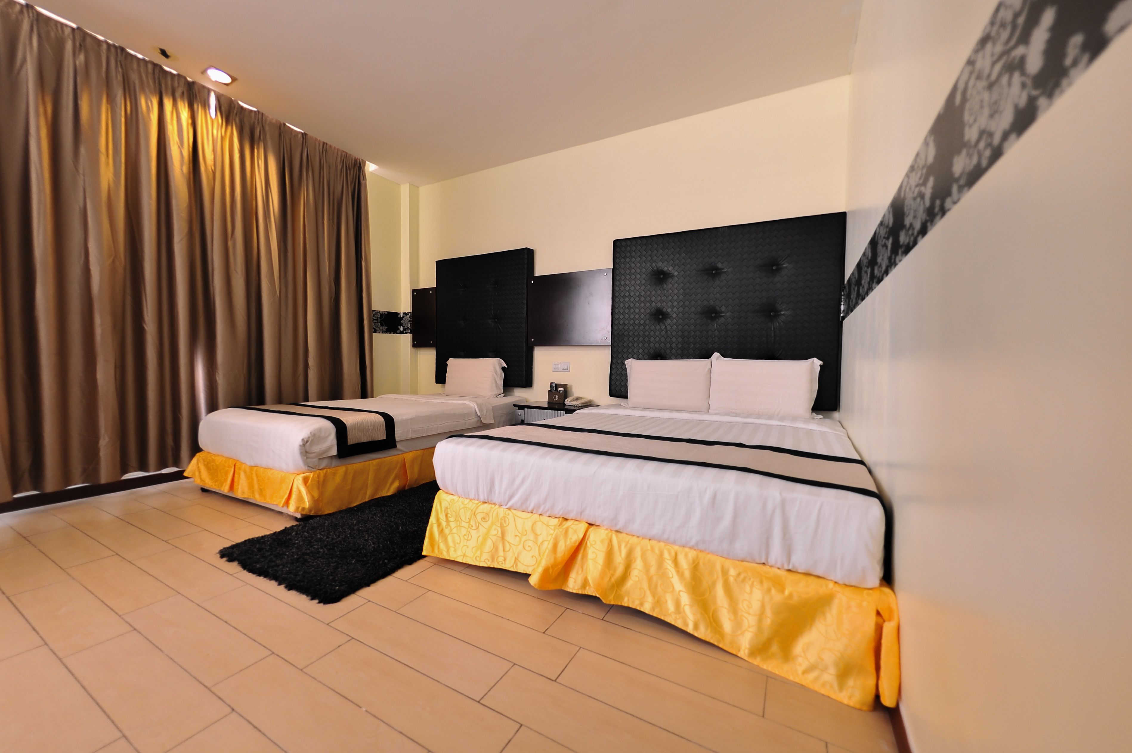 A hotel room with two beds, a black headboard, a white wall, and a black and yellow rug.