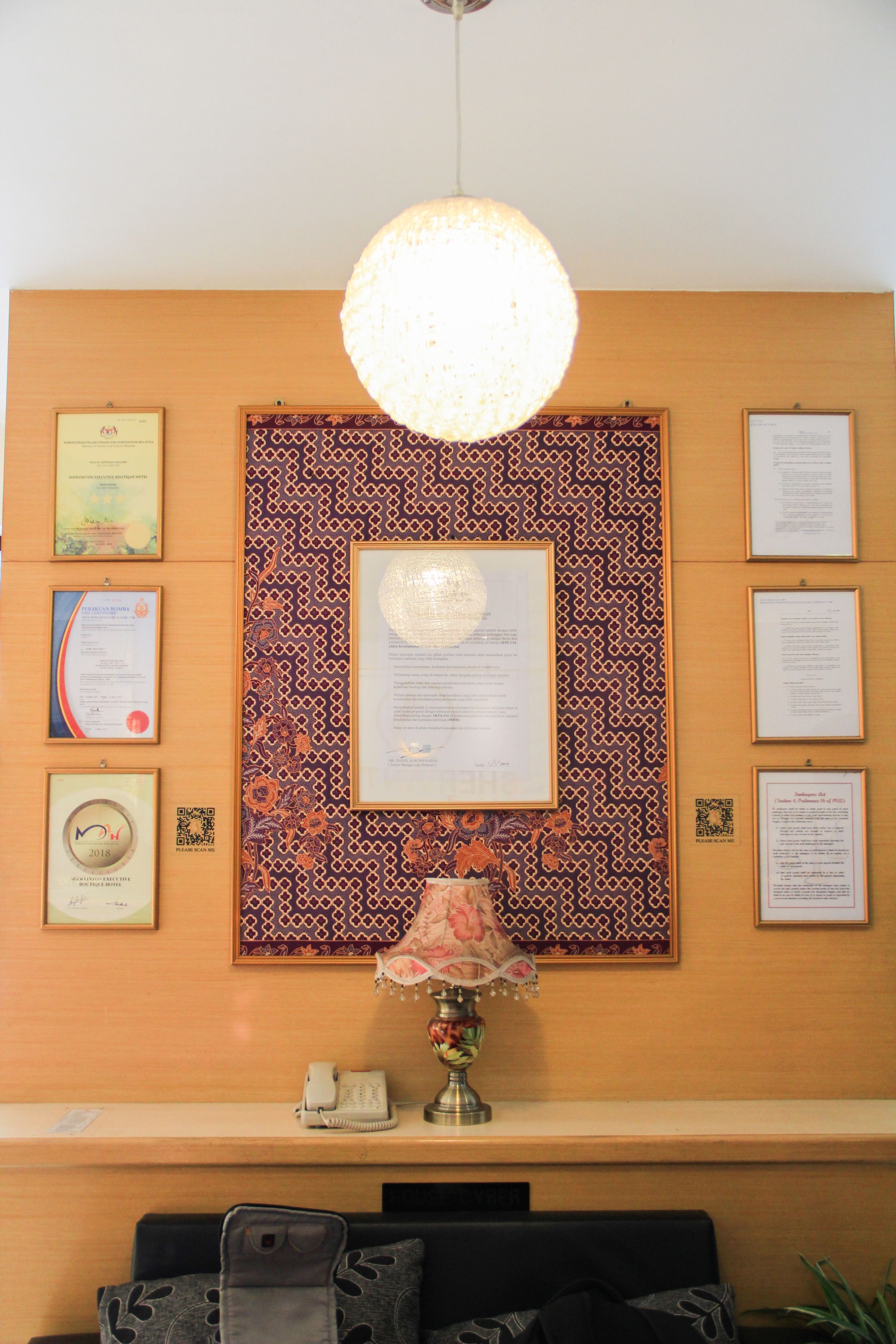 A reception desk with a lamp, framed certificates, and a patterned wall.