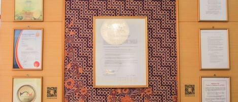 A reception desk with a lamp, framed certificates, and a patterned wall.