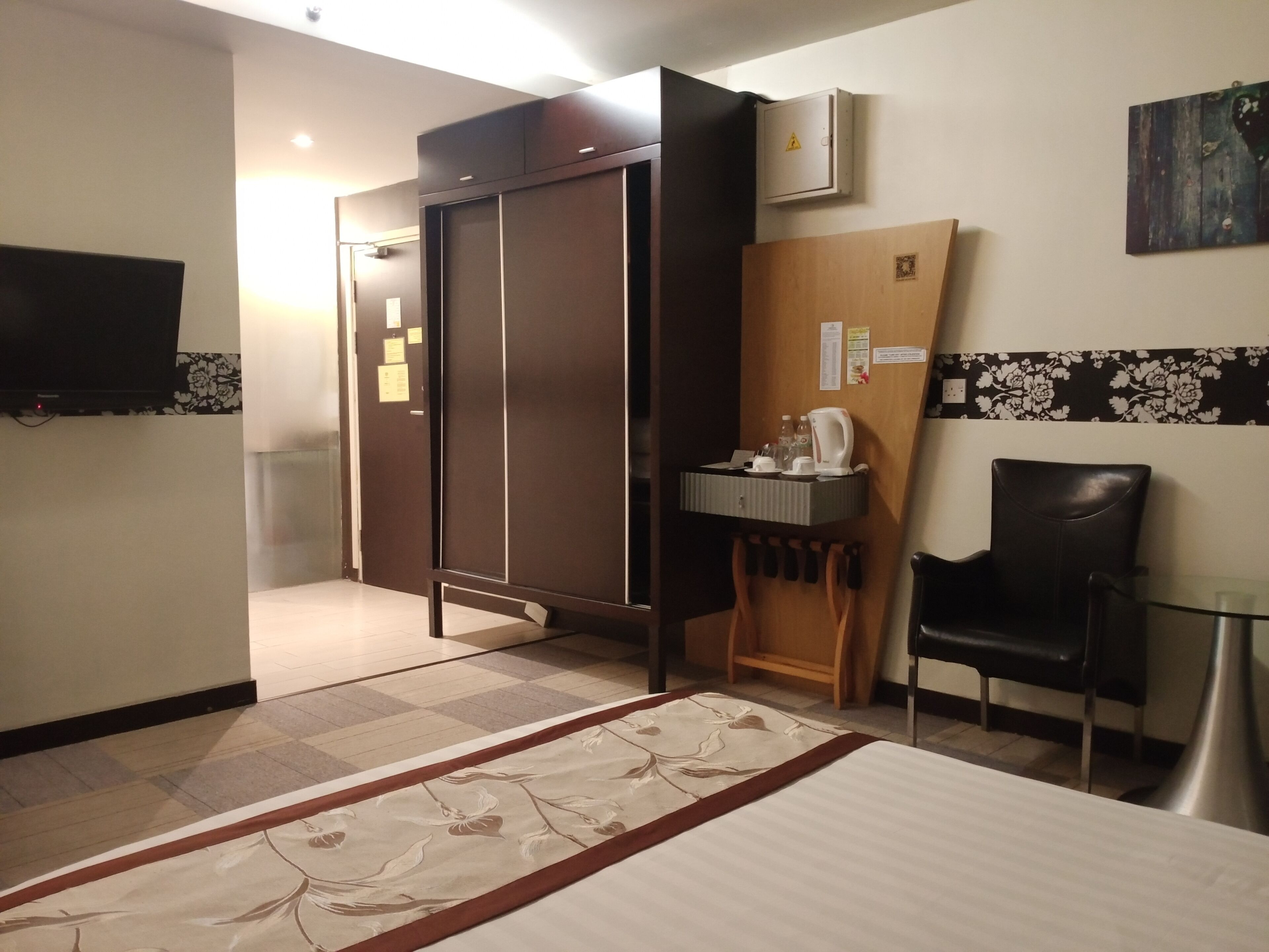 A hotel room with a bed, a desk with a chair, a wardrobe, a television, and a small cabinet.