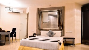 Una habitación de hotel con una cama, un escritorio, una silla, una mesita pequeña y un equipo de aire acondicionado.