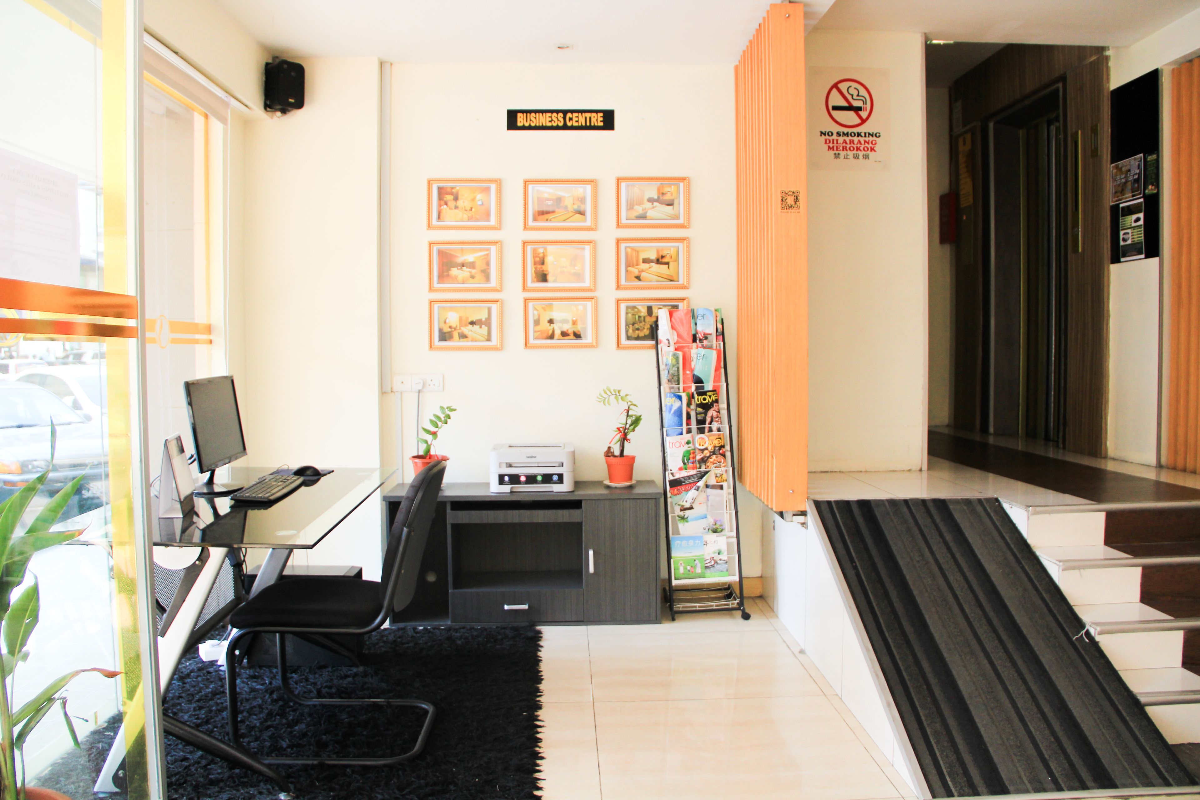 A business center with a desk, computer, and printer, a no smoking sign, and framed pictures on the wall.