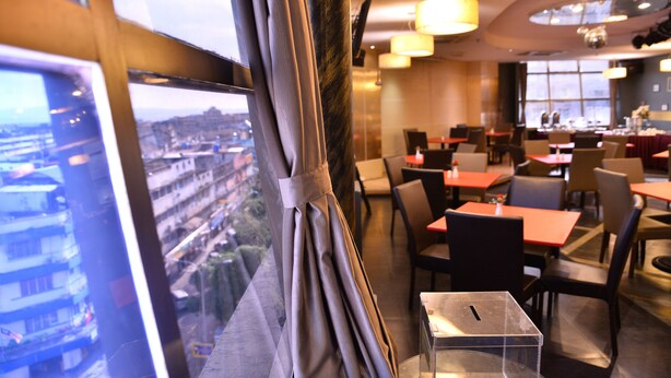 Un moderno comedor con mesas y sillas, un ventanal con cortinas y vistas a un paisaje urbano.