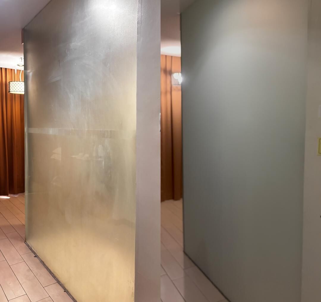 A hallway with a frosted glass partition, wooden flooring, and a door with a light switch.