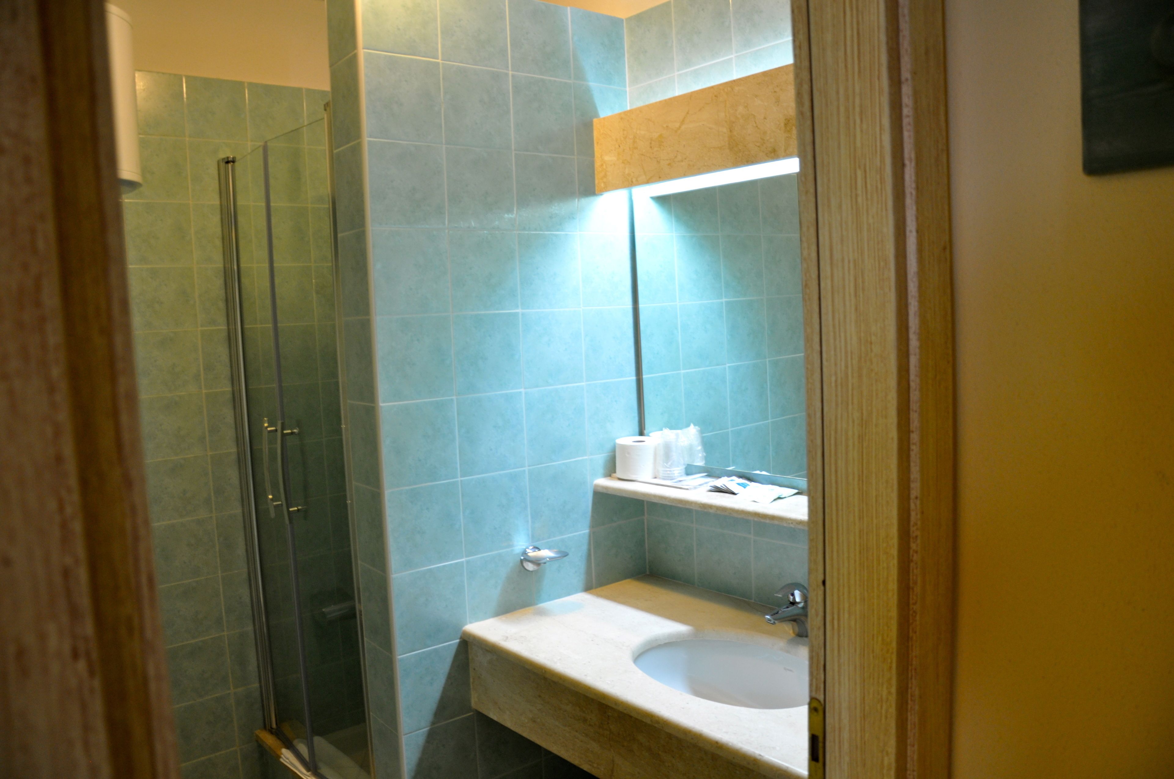 A bathroom with a glass shower enclosure, a sink, and a mirror.