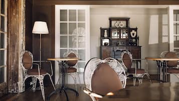 Zona pranzo con sedie e tavoli decorati, una lampada vintage e un armadietto in legno con vetrate.