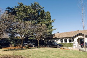 A residential house with a well-maintained lawn, three parked cars, and mature trees. - Links House (Burradoo)