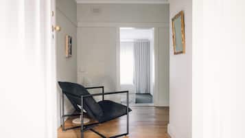 A hallway with a black chair, a framed picture, and a window with curtains.