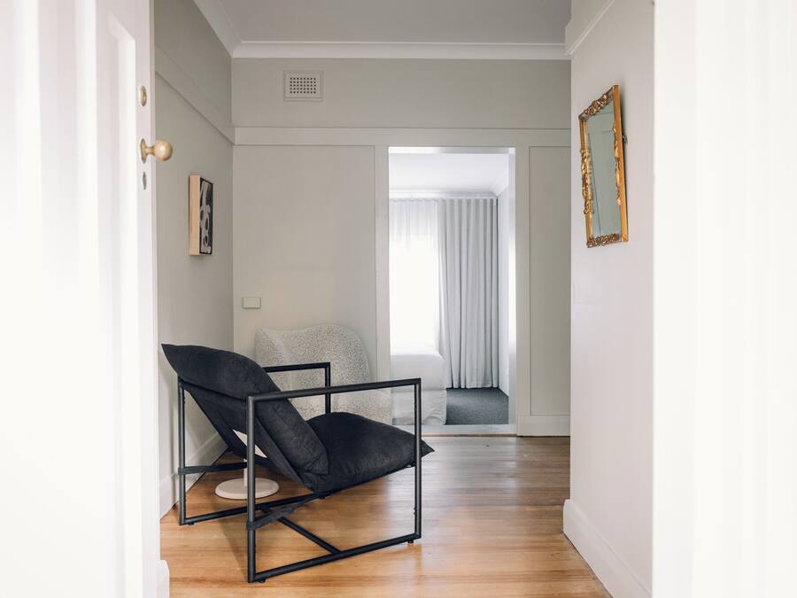 A hallway with a black chair, a framed picture, and a window with curtains.
