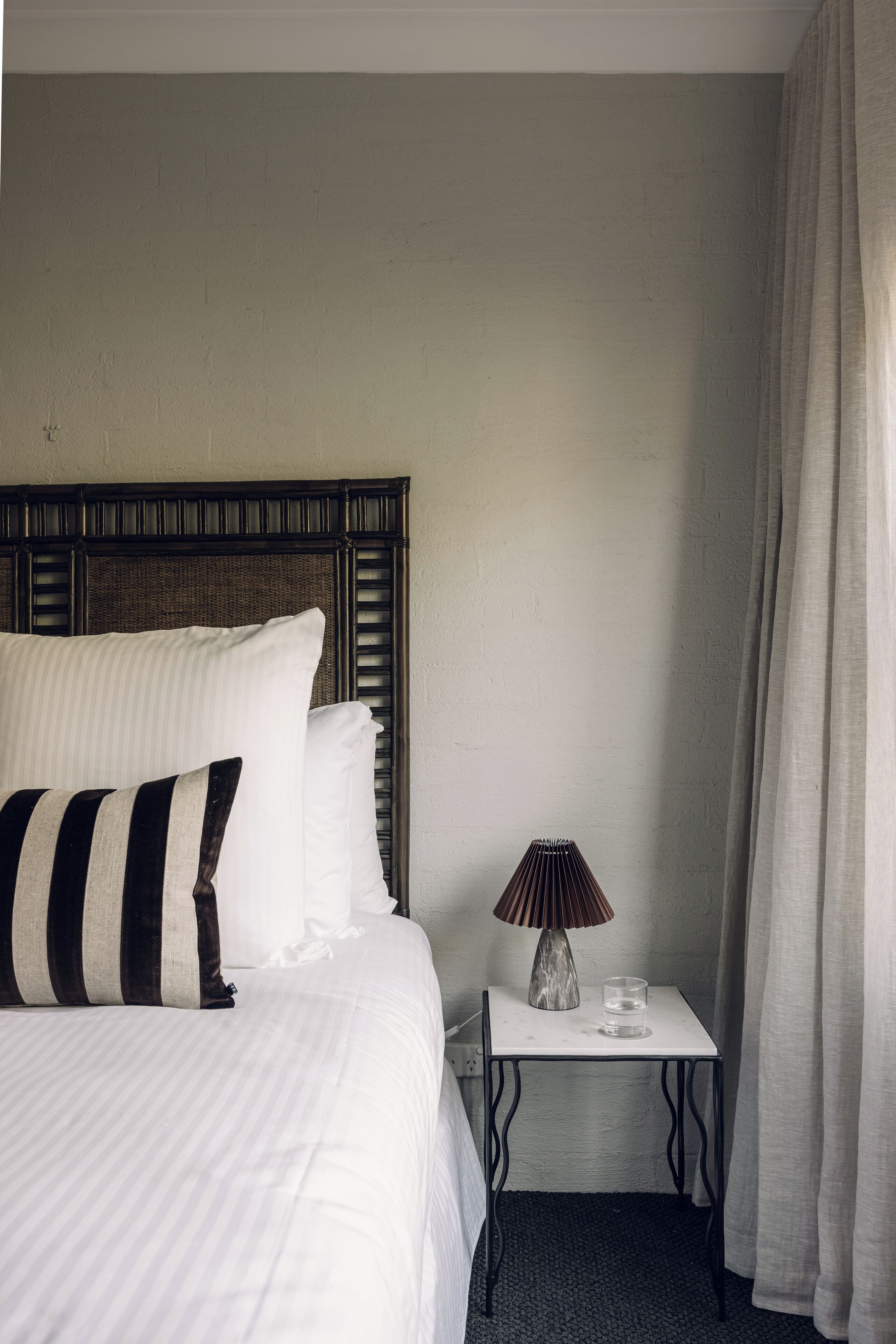 A neatly made bed with striped pillows, a bedside lamp, and a glass on a small table beside it.