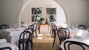 A dining area with tables set for a meal, chairs, and a vase with branches on a table. - Links House (Burradoo)
