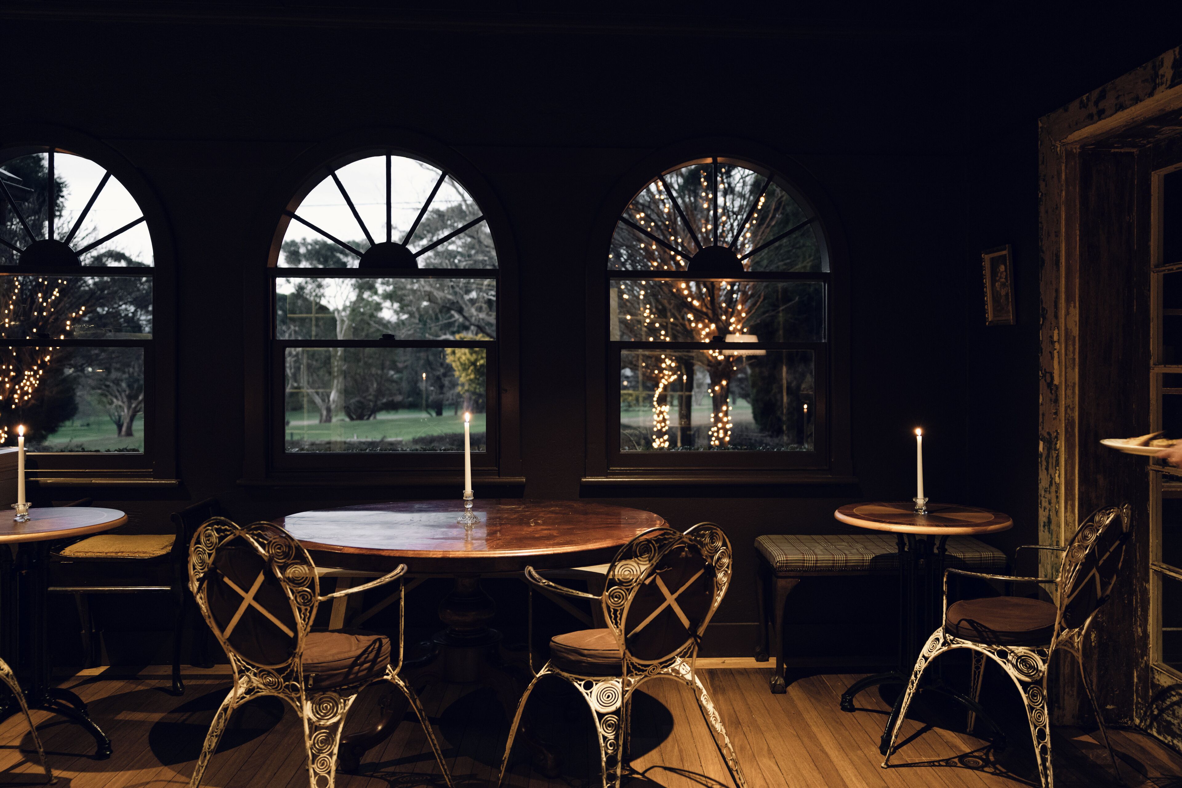 A dimly lit room with three arched windows, a round wooden table, and ornate chairs.