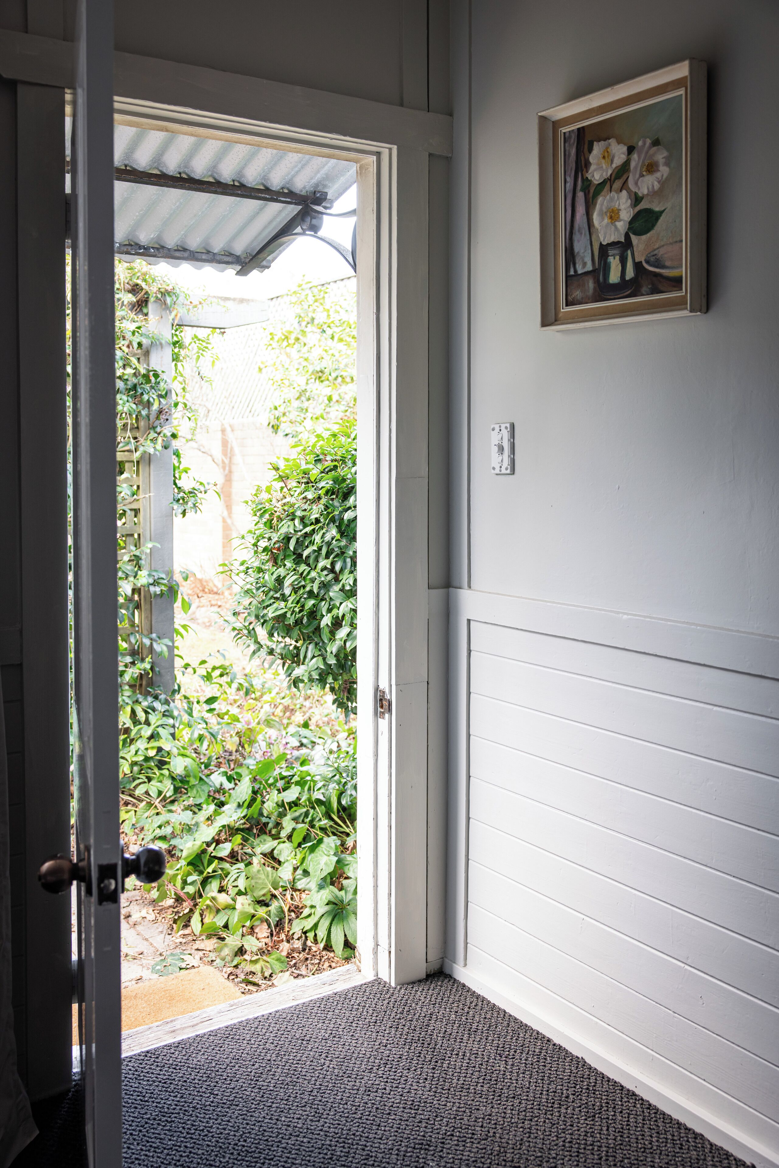 A doorway leading to a garden with a door and a framed painting on the wall.