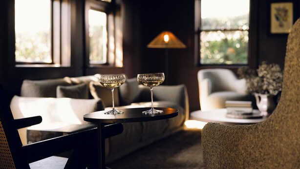 A cozy room with a sofa, a round table with two glasses of wine, and a lamp. - Links House (Burradoo)