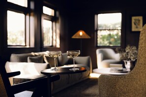 A cozy room with a sofa, a round table with two glasses of wine, and a lamp. - Links House (Burradoo)