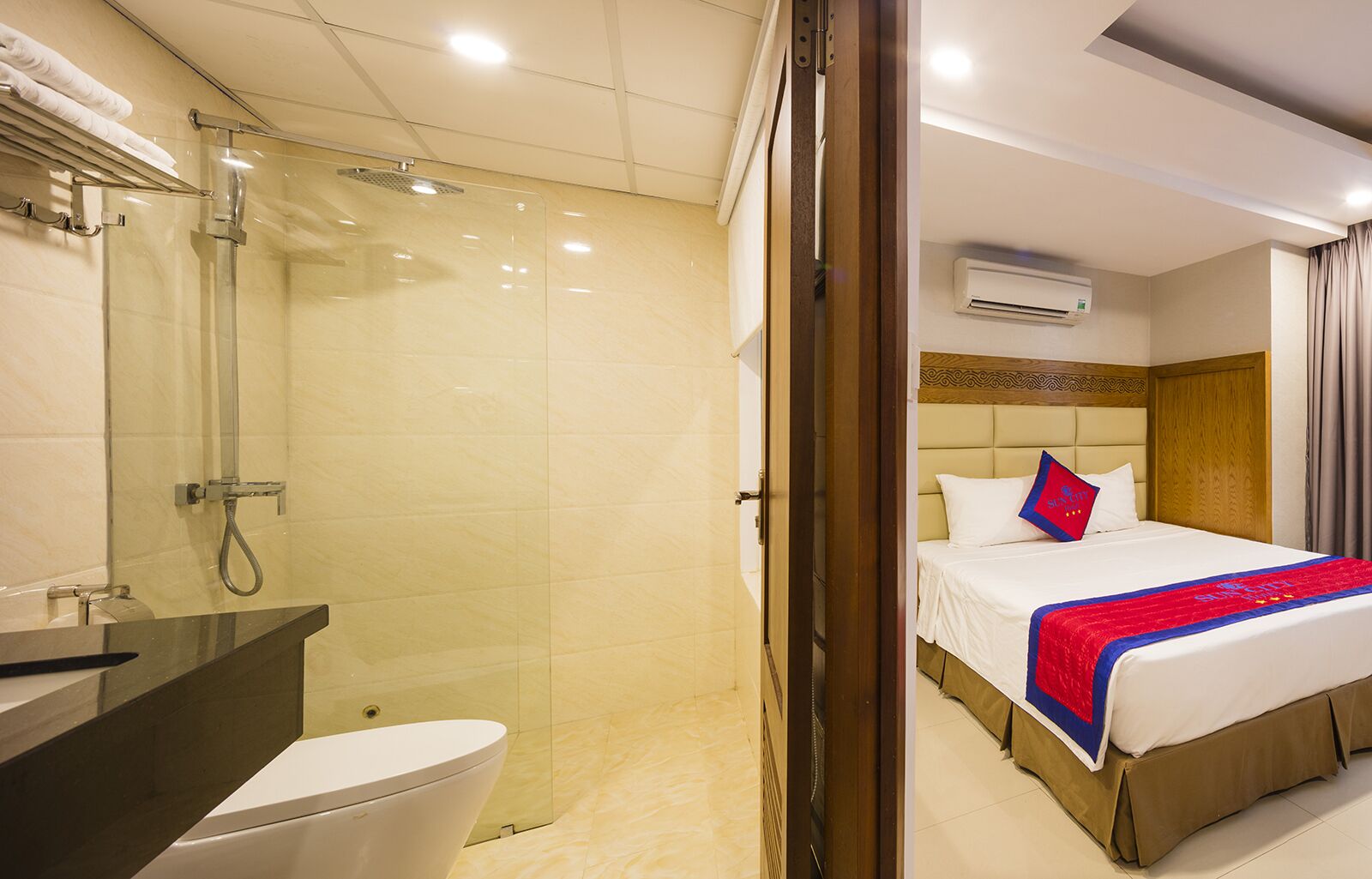 Une chambre d’hôtel avec une douche, des toilettes et un lit recouvert d’une couverture rouge et bleue.